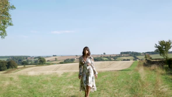 Young woman in long floral dress walks towards the camera, catwalk style.