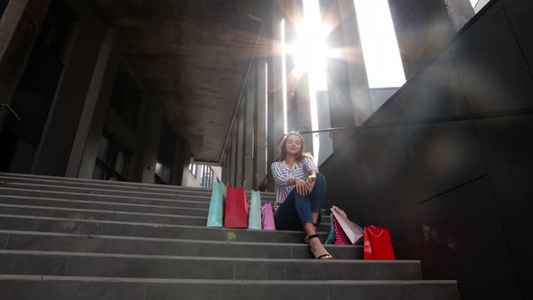 Teenager Smiling Girl with Shopping Bags Sitting on Stairs Near Shopping Mall. Black Friday Sale