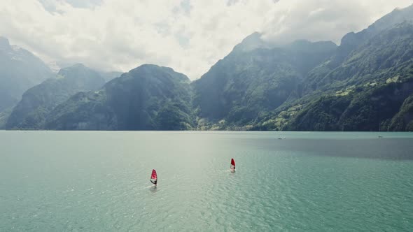 Two Men are Windsurfing on a Lake at the Foot of the Alps in Switzerland