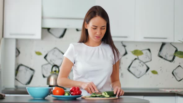 Happy Young Housewife Cutting Fresh Cucumber in the Cozy Kitchen