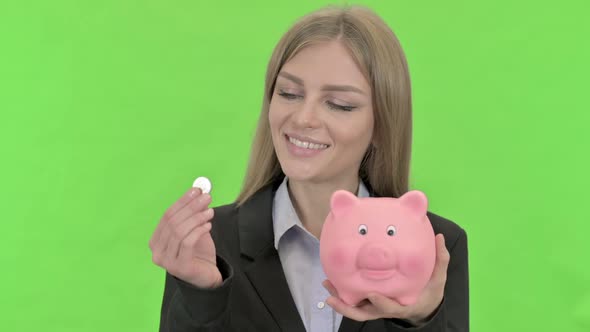 Businesswoman Inserting Coin in Piggy Bank Against Chroma Key