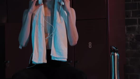 A Young Pretty Woman Sitting in Locker Room with a Towel and Headphones on Her Neck