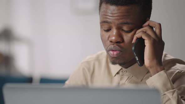 Black Man is Communicating By Mobile Phone Sitting at Home and Working with Laptop Closeup Portrait