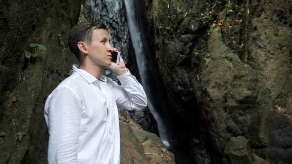 Serious Guy Talks on Smartphone at Tropical Waterfall