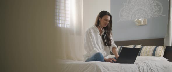 A young woman speaking to someone through earphones while working on her laptop