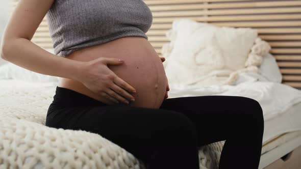 Unrecognizable woman in advanced pregnancy sitting on bed and feeling strong backache. Shot with RED