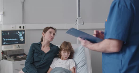 Senior Male Doctor Discussing Over Report with Mother and Son in Ward at Hospital