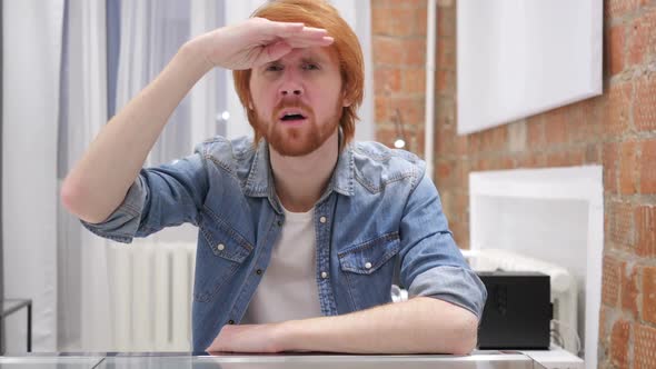 Searching Gesture By Redhead Beard Man Sitting in Office