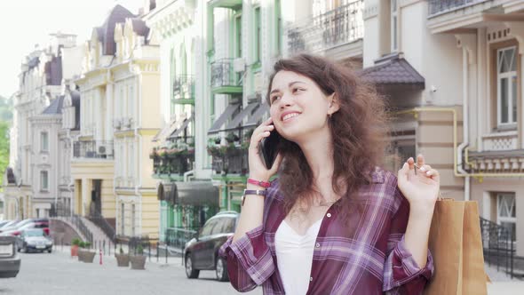 Charming Young Woman Talking on the Phone on City Street Holding Shopping Bags