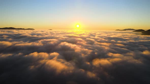 Aerial View of Colorful Sunrise Over White Dense Fog with Distant Dark Silhouettes of Mountain Hills