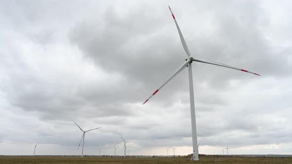 Large wind turbines with blades in the wind park on the background cloudy sky.