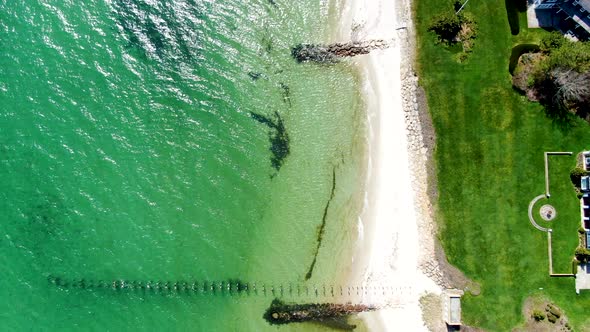 Remains of old pier and crystal clear ocean water near sandy coastline, aerial view