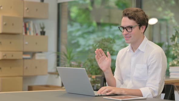 Young Man Talking on Video Call on Laptop in Modern Office