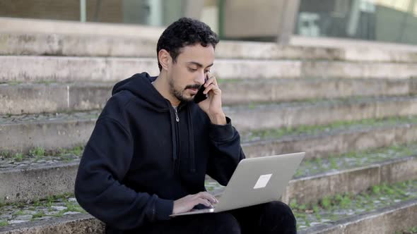 Man Using Laptop and Talking By Smartphone