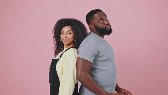 Young Smiling African American Couple Standing Back to Back and Pointing Fingers Up Purple Studio