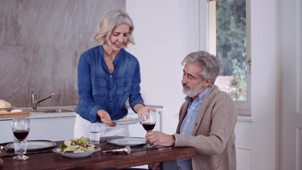 Slow motion shot of mature woman serving dinner to her husband