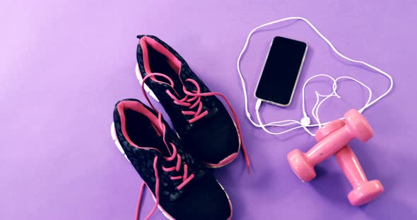 Mobile phone with headphones, shoes and dumbbells on table