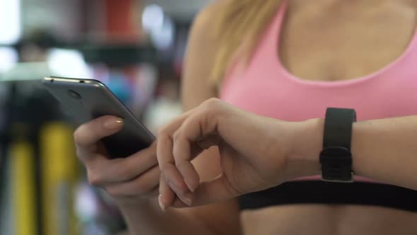 Girl Connecting Smartphone to Her Smart Watch in Gym Before Sports Exercising