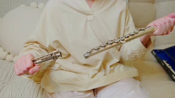 A woman hand with a flute is playing at home on the sofa in the living room, close-up