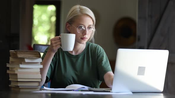 Blonde girl in glasses working with notebook at home as freelancer