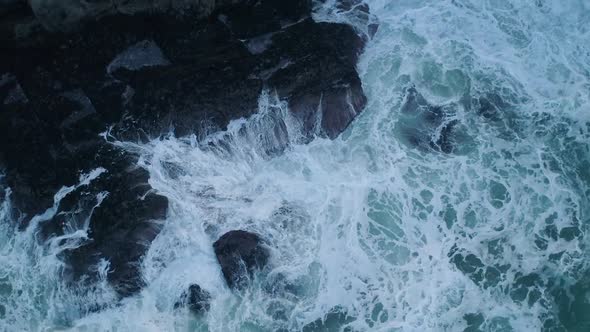 top down aerial of waves crashing against rocks