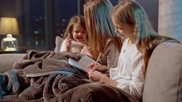 Mother Sitting on Sofa with Daughters and Drawing in Albums