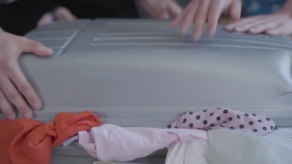 Man's and Woman's Hands Trying To Pack a Suitcase Before Travel