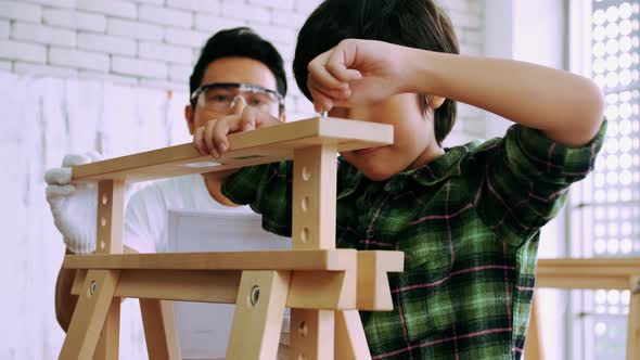 Young male carpenter teaching his son how to work with wood in workshop.