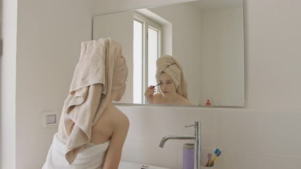 Teenage girl applying mascara in front of the bathroom mirror