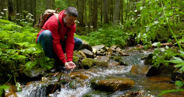 A Bearded Man with a Backpack Drinks Water From a Mountain Stream