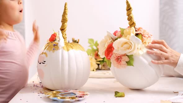 Little girl and her mother painting face of a unicorns on her craft pumpkin for Halloween.