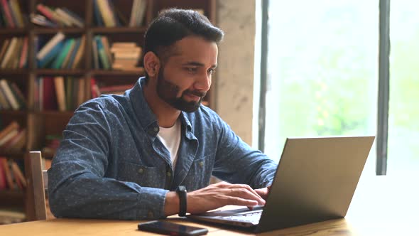 Positive Indian Male Freelancer Looks at the Laptop Monitor