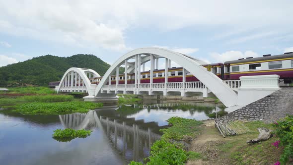 A train crossing on Tha Chomphu White Bridge, Lamphun, Thailand with lake or river