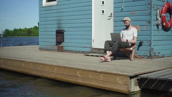 Bearded Guy Hipster is Working with Laptop and Having Nice Day at Lake Pier on Summer Spbd