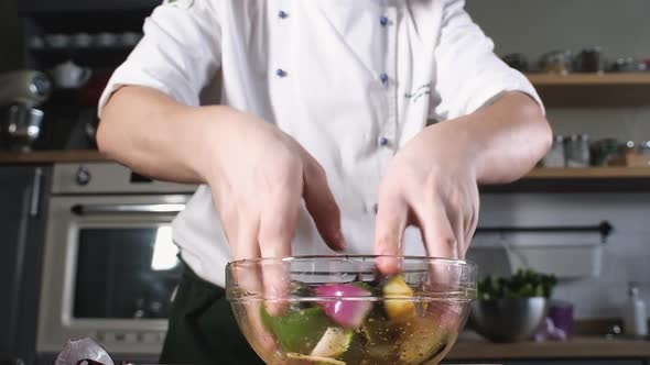 chef in kitchen of  restaurant mixes vegetables with olive oil with hands.