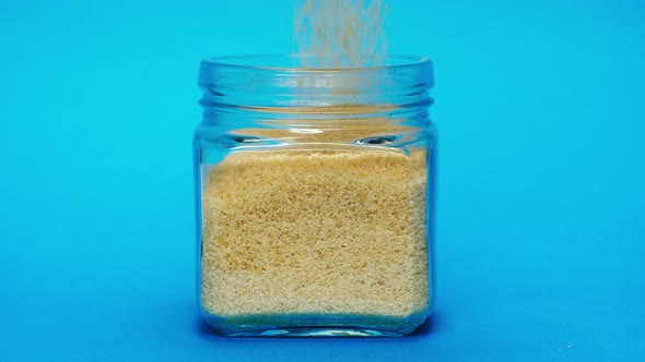 Closeup of Falling Down Wheat Into Glass Jar on Blue Background