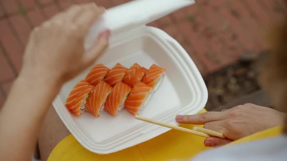 Opens the Package with Rolls and Sushi and Hands Takes Them