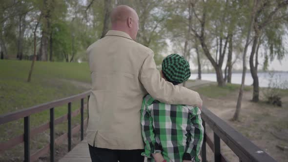 Back View of Grandfather and Grandson Walking on the Bridge in the Park with Their Backs