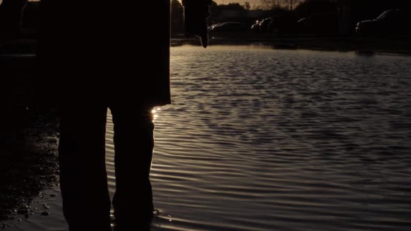 Silhouette of person walking in ripples in water at sunset