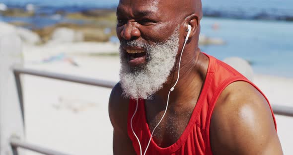 Tired senior african american man wearing headphones taking a break from running on promenade