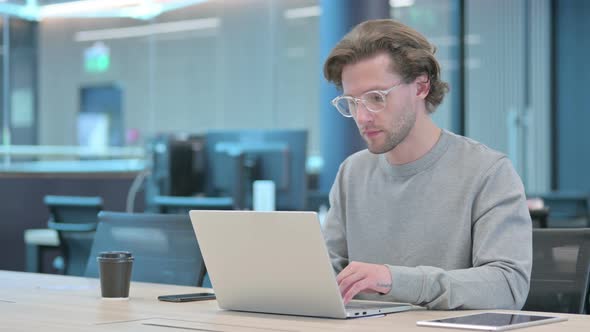 Thumbs Up By Young Businessman with Laptop at Work