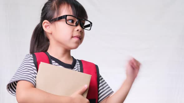 Smiling schoolgirl wearing casual outfit with backpack holding books and pointing empty