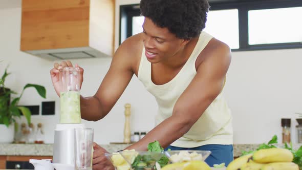 Fit african american man cooking, preparing healthy green smoothie