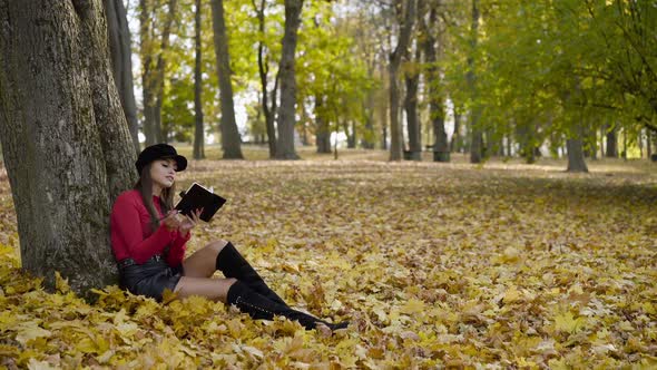 Creative Girl Resting in Autumn Park and Writing Down Thoughts in a Notebook