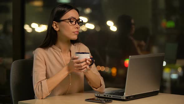 Female Freelancer Drinking Coffee and Editing Project on Laptop