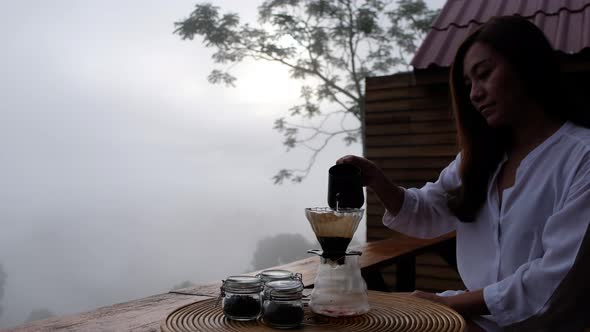 A woman making drip coffee with a beautiful nature view on foggy day