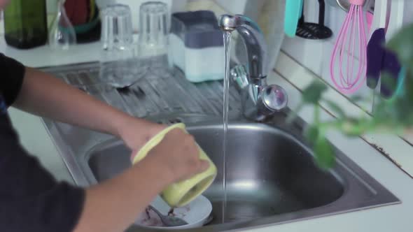 Man washing dishes under running warm water in the kitchen after eating