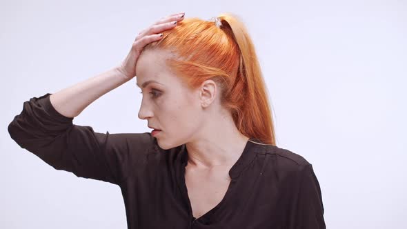 Middleaged Caucasian Female with Colored Orange Hair and Dark Brown Shirt Holding Head with Hands in