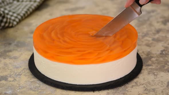 Fruit cake with peach, jelly and mousse. Woman hands cutting peach mousse cake.	