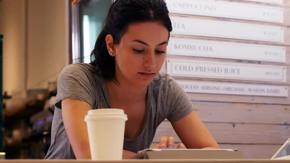 Woman with cup of coffee using digital tablet on table